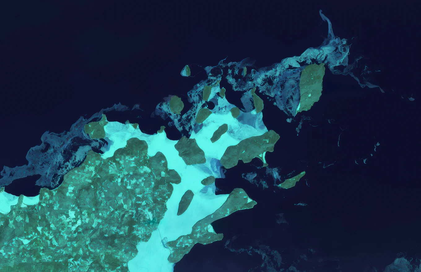 A top-down satellite image of a green peninsula and surrounding archipelago against dark blue ocean.